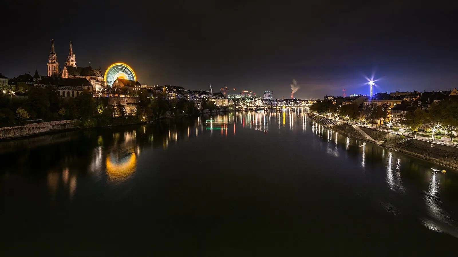 Basel bei Nacht während der Herbstmesse: Rhein mit Spiegelungen, links Münster und beleuchtetes Riesenrad